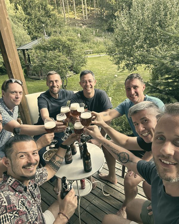 Männer stoßen auf einer Terrasse lachend mit ihren Gläsern an.