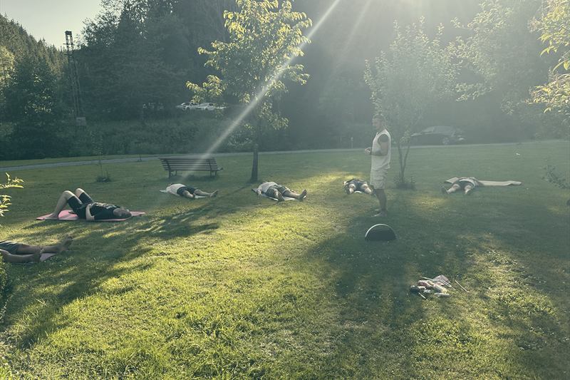 Männer liegen auf Matten im Gras, die Sonne fällt schräg durch die Bäume.