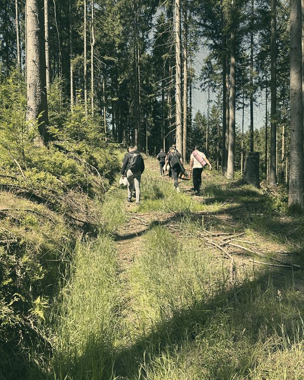 Ein schmaler Waldweg, weit vorn gehen ein paar Männer zwischen den Bäumen.