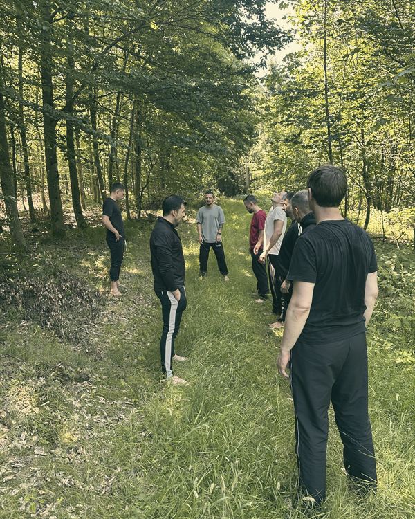 Männer stehen sich auf einer Waldlichtung im Kreis gegenüber.