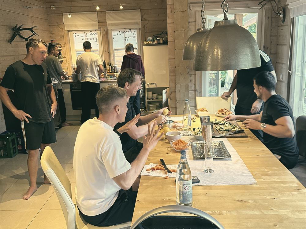 Männer bereiten in einer hellen Holzküche gemeinsam das Essen zu.