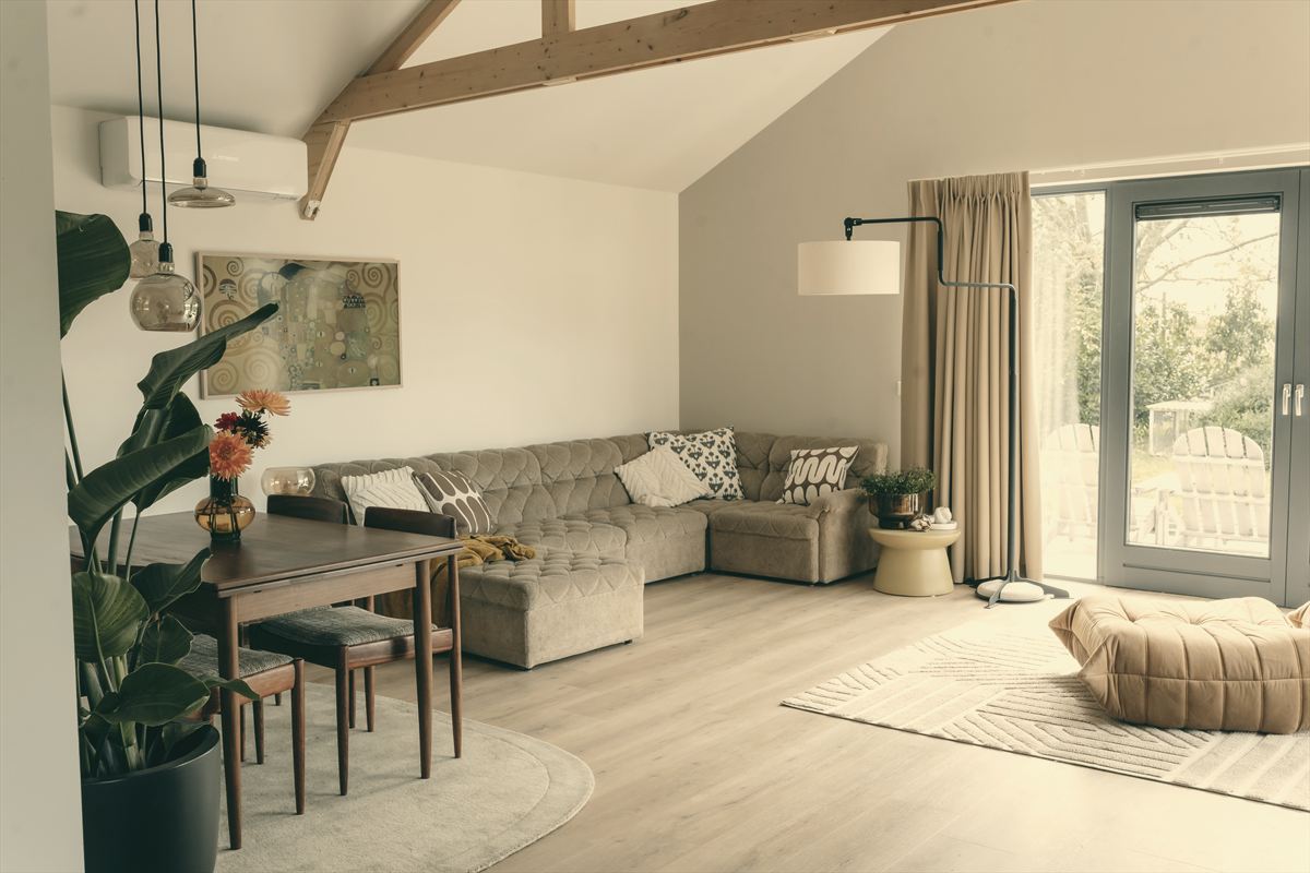 Wohnbereich mit Sofa, Esstisch und Pflanzen, durch die Glastür der Garten.