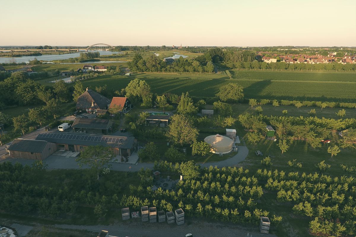 Die Anlage aus der Vogelperspektive: Obstwiesen, Jurte und Häuser, am Horizont Fluss und Brücke.