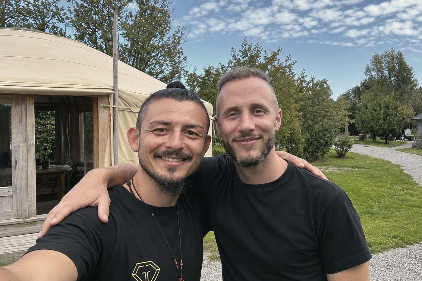 Dorje und Alexander stehen Arm in Arm vor einer Jurte und lächeln in die Kamera.